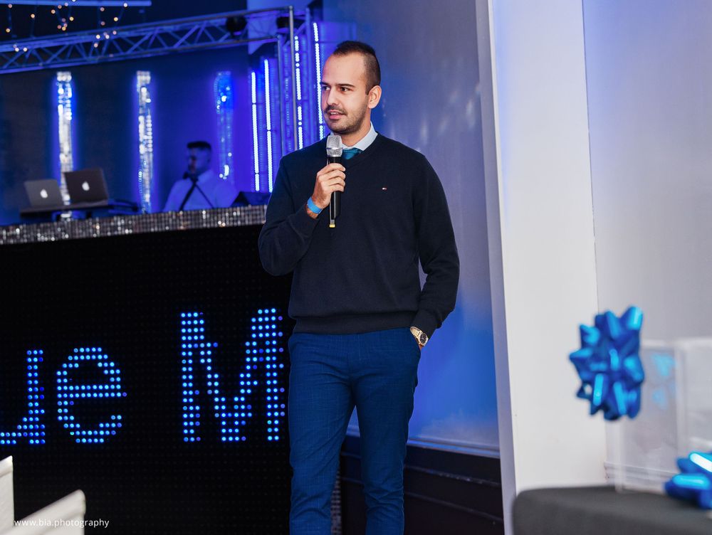 Speaker presenting on stage with blue LED lighting and promotional display.