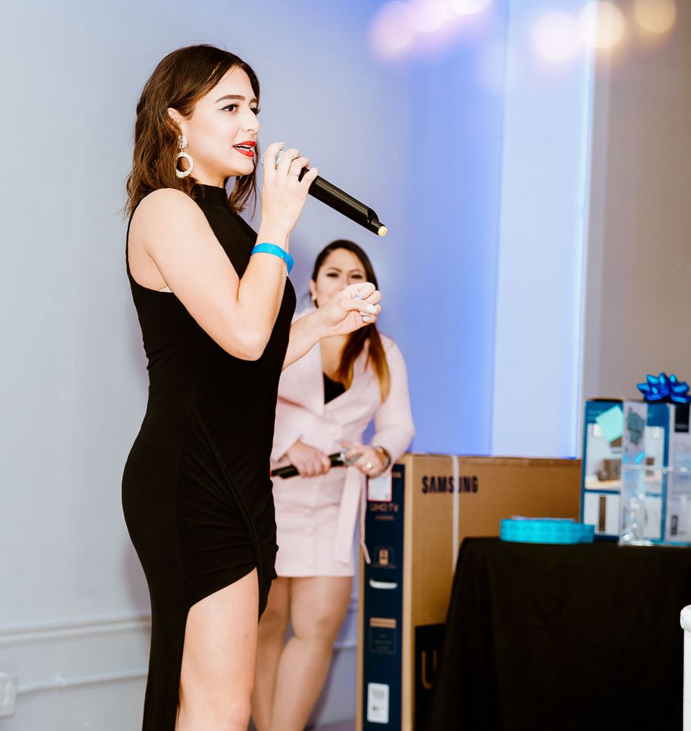 Woman in black dress singing on microphone at corporate event with decorative backdrop.