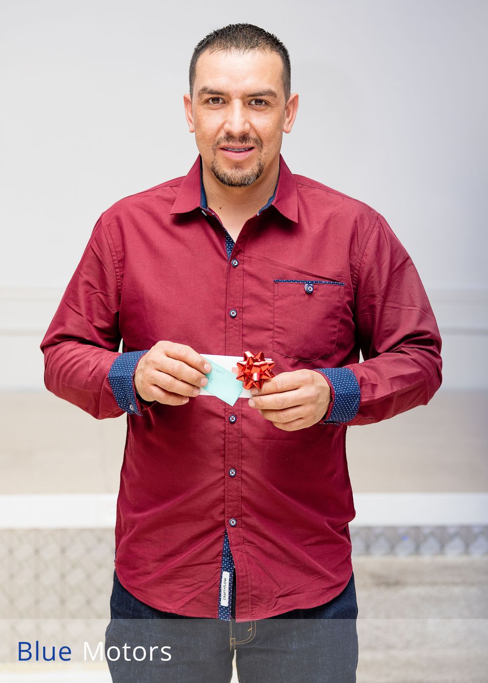 Man in red button-down shirt holding something small against gray background.