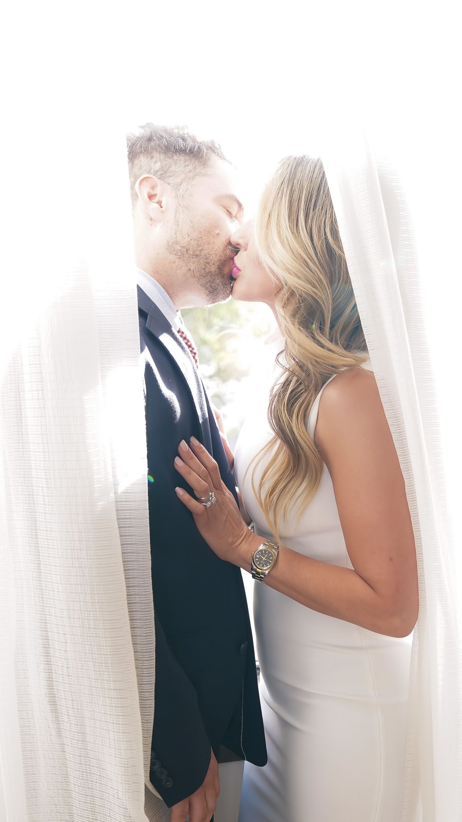 Romantic wedding photography of a couple in formal attire sharing an intimate moment behind a sheer curtain.
