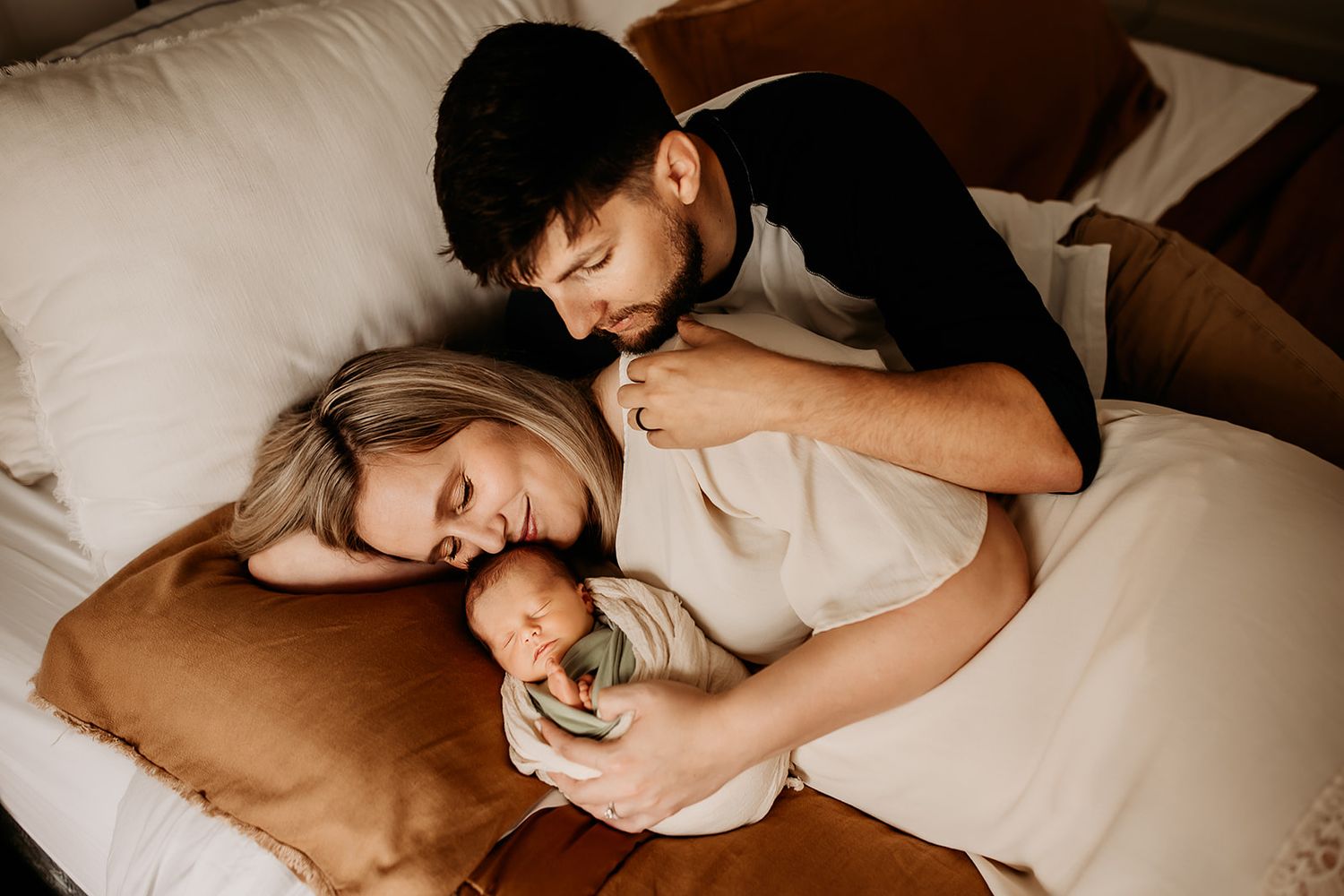 A mother and father snuggle on their bed with their newborn baby boy during their in home newborn session.