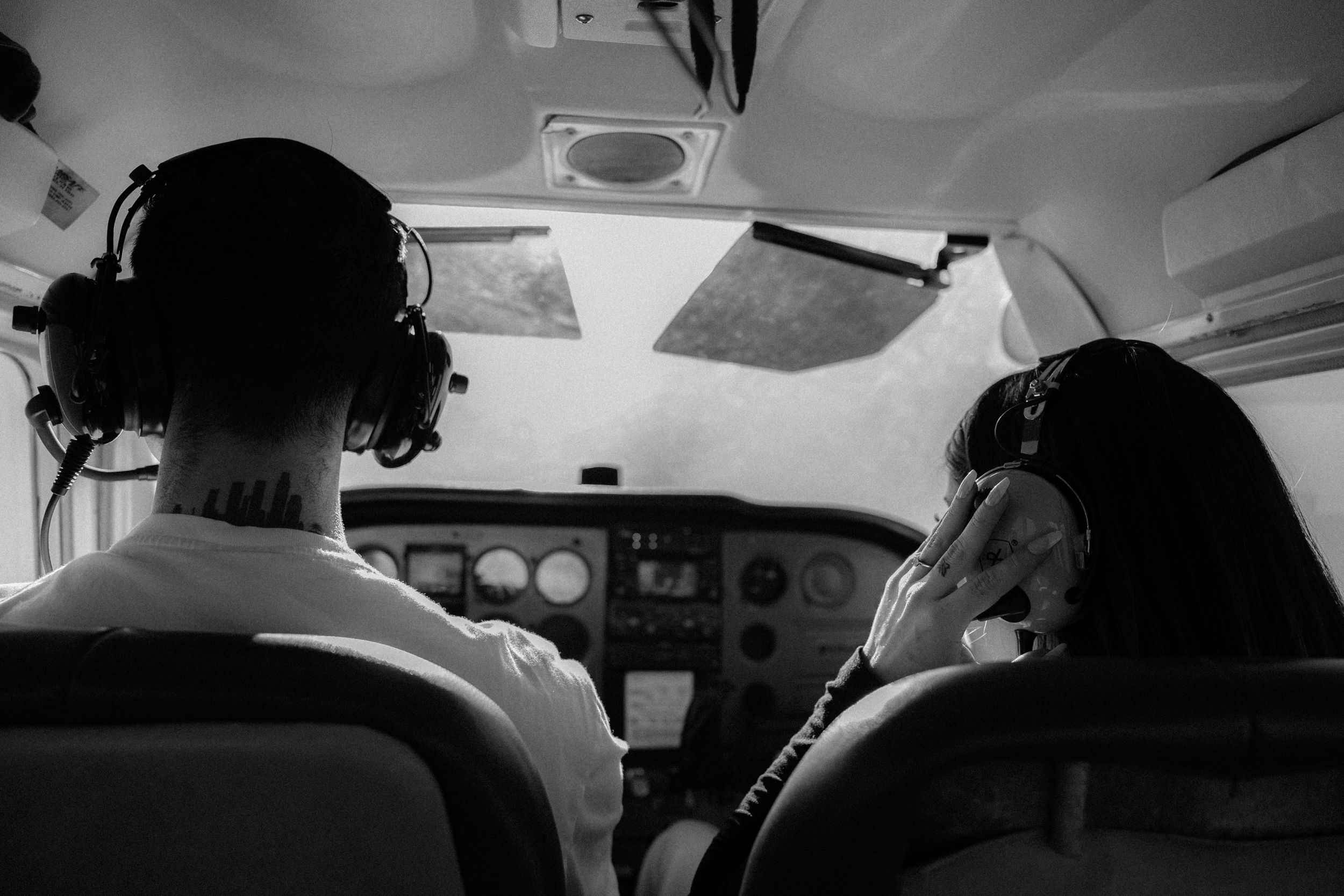 Two pilots wearing headsets flying small aircraft together, black and white photo.
