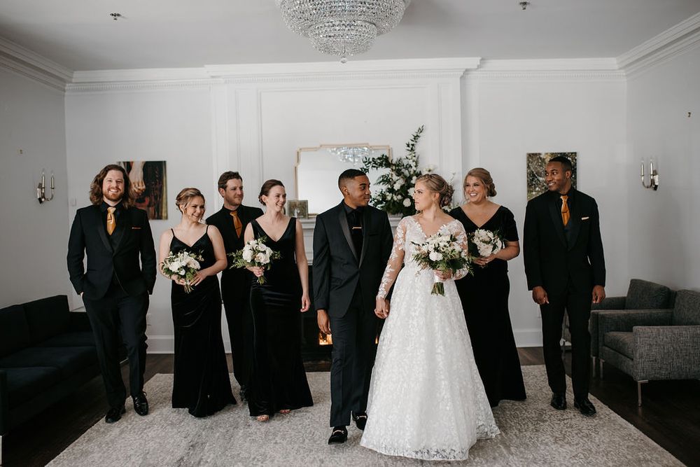 Wedding party in black walking together with bride in white lace gown in bright room.