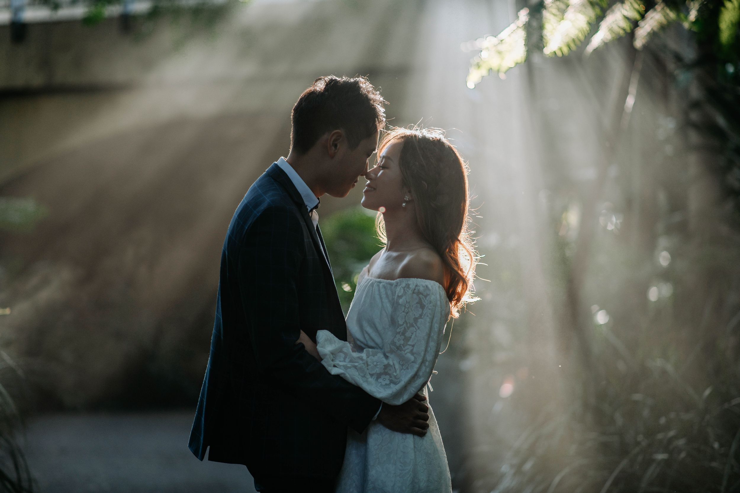 A romantic couple embraces in dramatic sunbeams filtering through greenery.