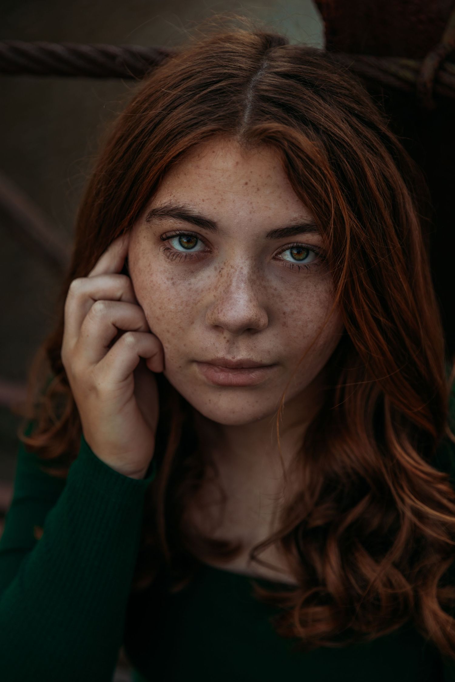 Portrait of a young woman with red hair, freckles and striking blue eyes wearing a green sweater.