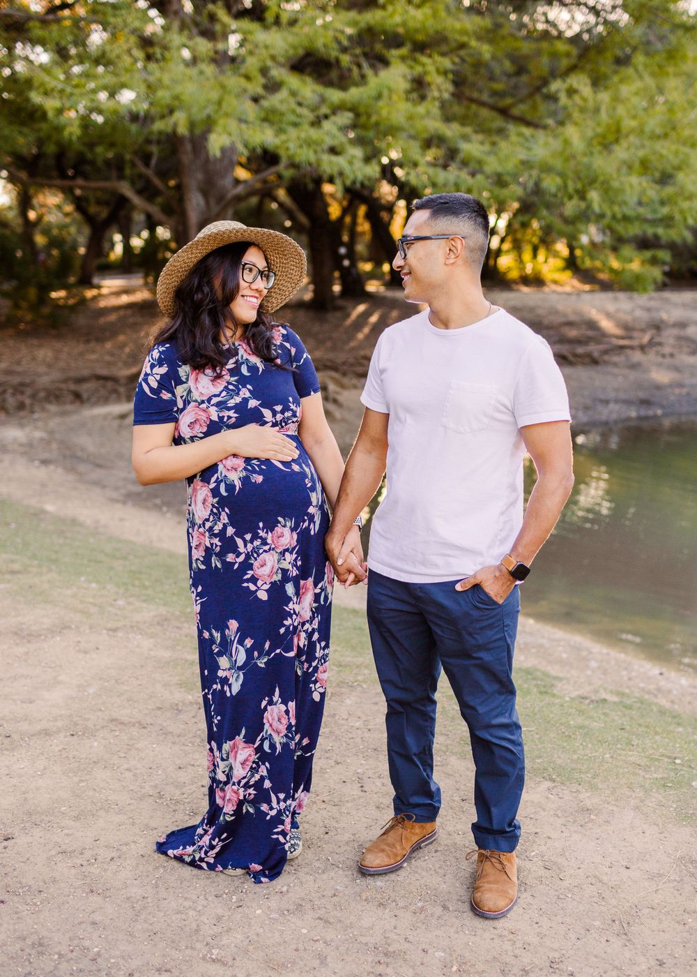 Couple holding hands by waterfront with person wearing floral maternity dress.