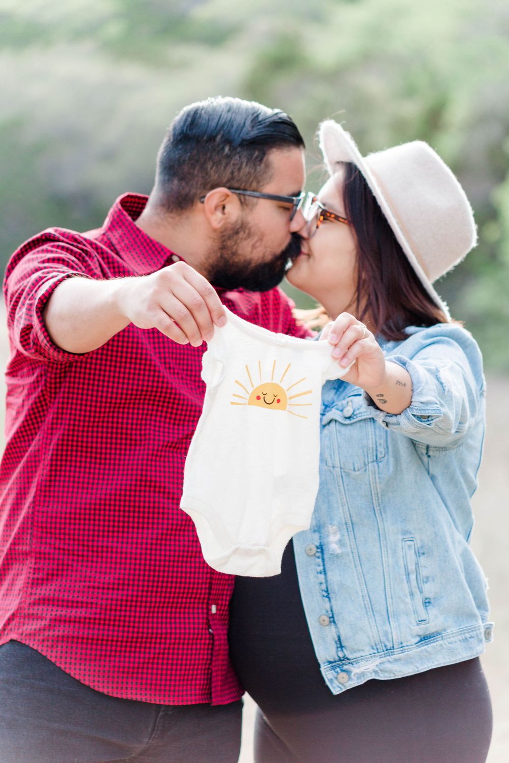 Couple sharing intimate moment while holding baby onesie outdoors.