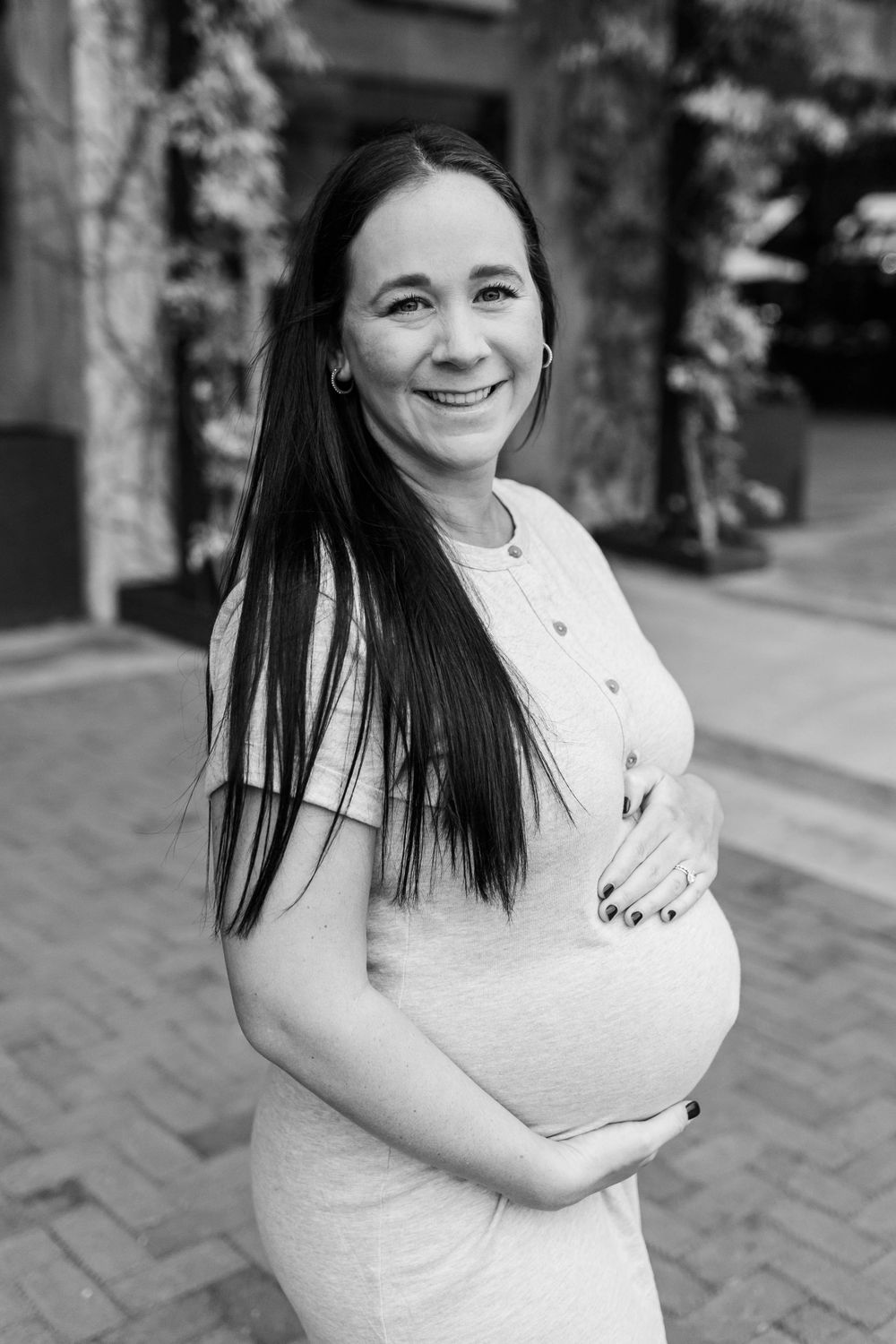 Black and white portrait of a pregnant person in a light dress smiling outdoors.