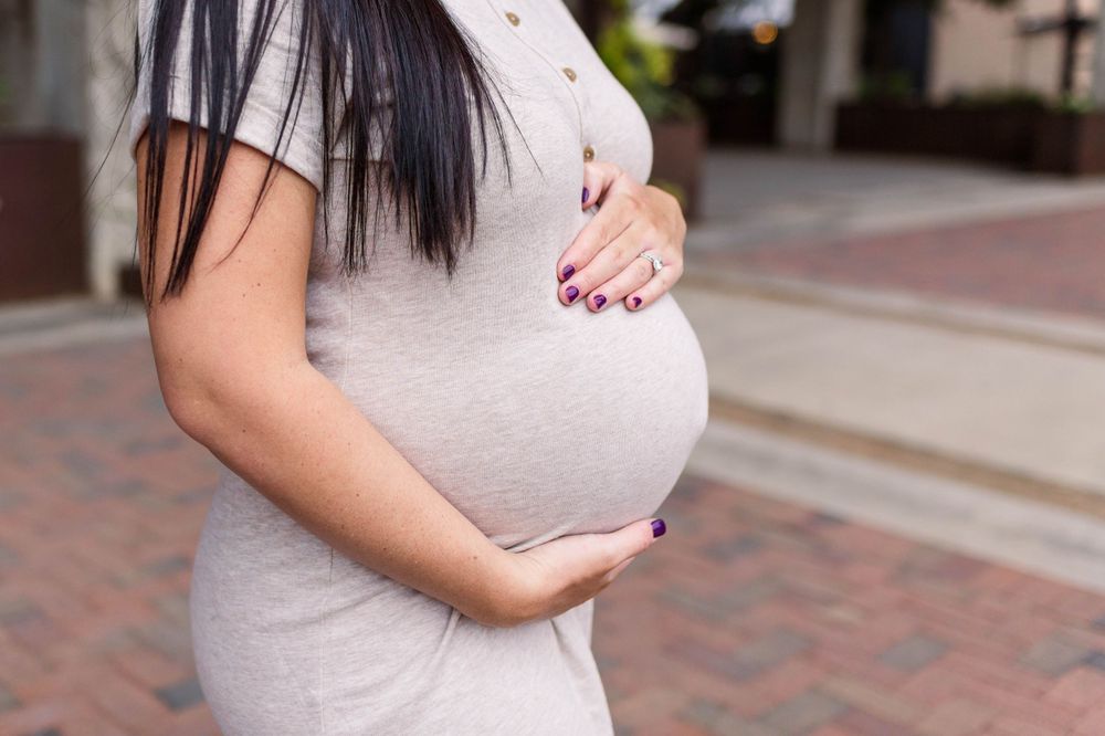 Close-up of hands cradling a pregnant belly in a light colored dress.