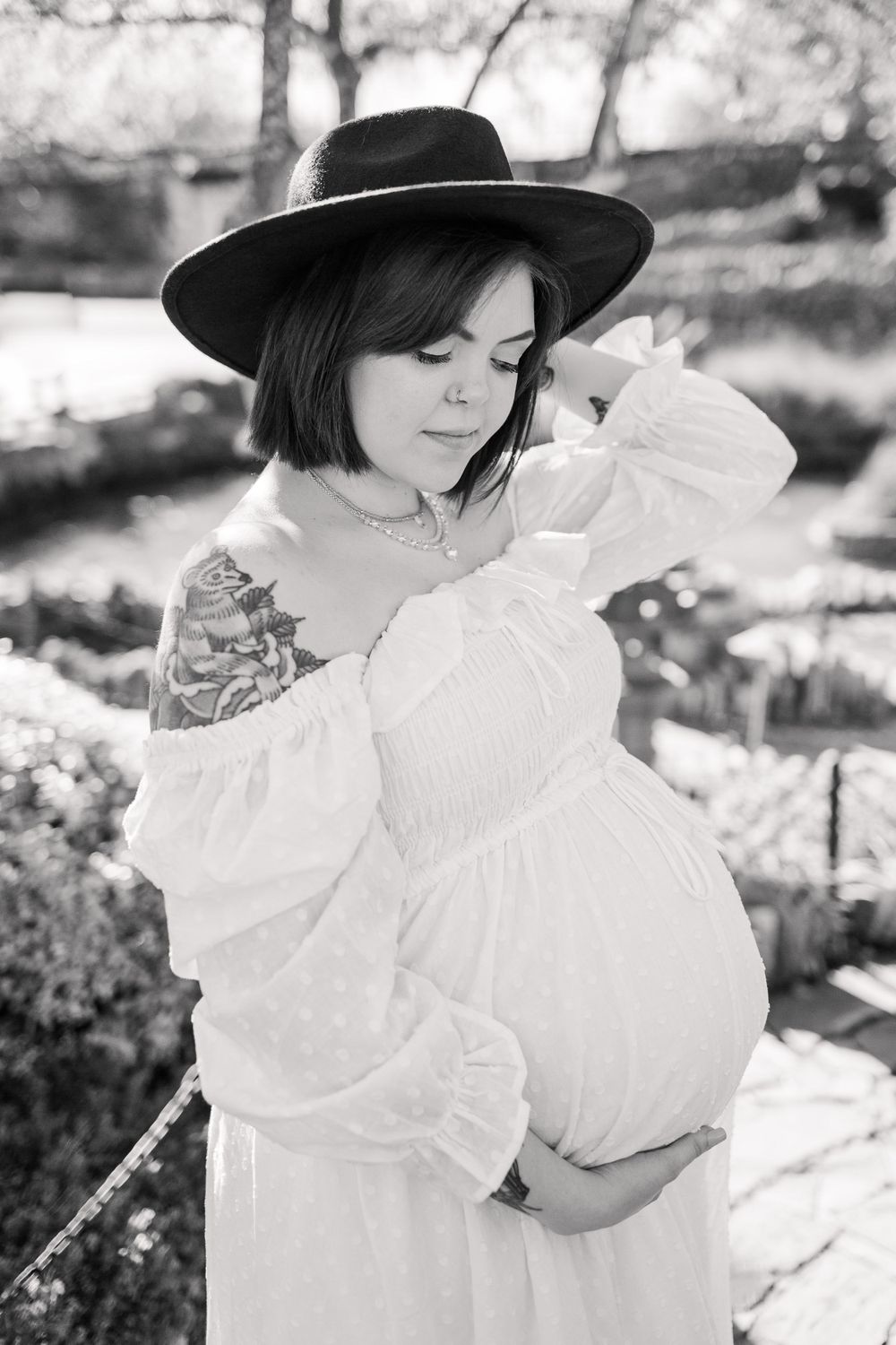 Black and white maternity photo with person wearing wide brim hat and flowy white dress.