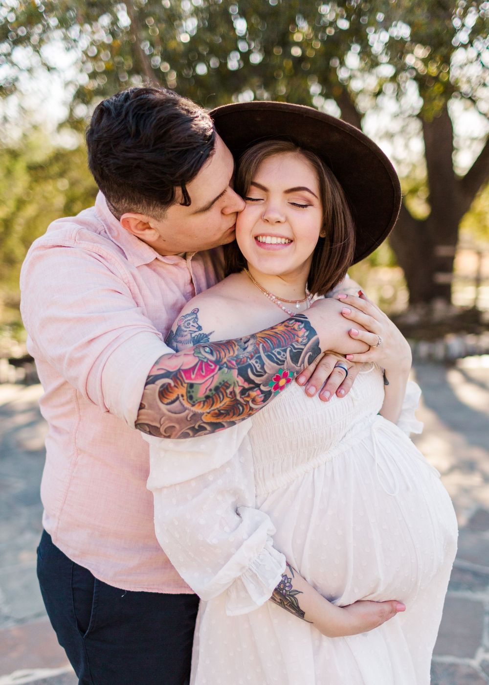 Sweet maternity moment captured with couple embracing in sunlit outdoor setting.