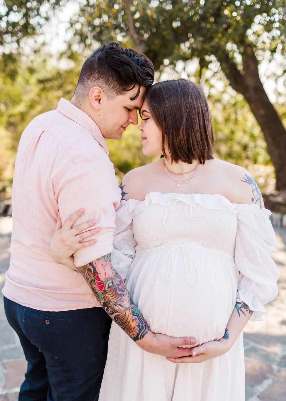 Intimate maternity moment between couple touching foreheads in outdoor setting.