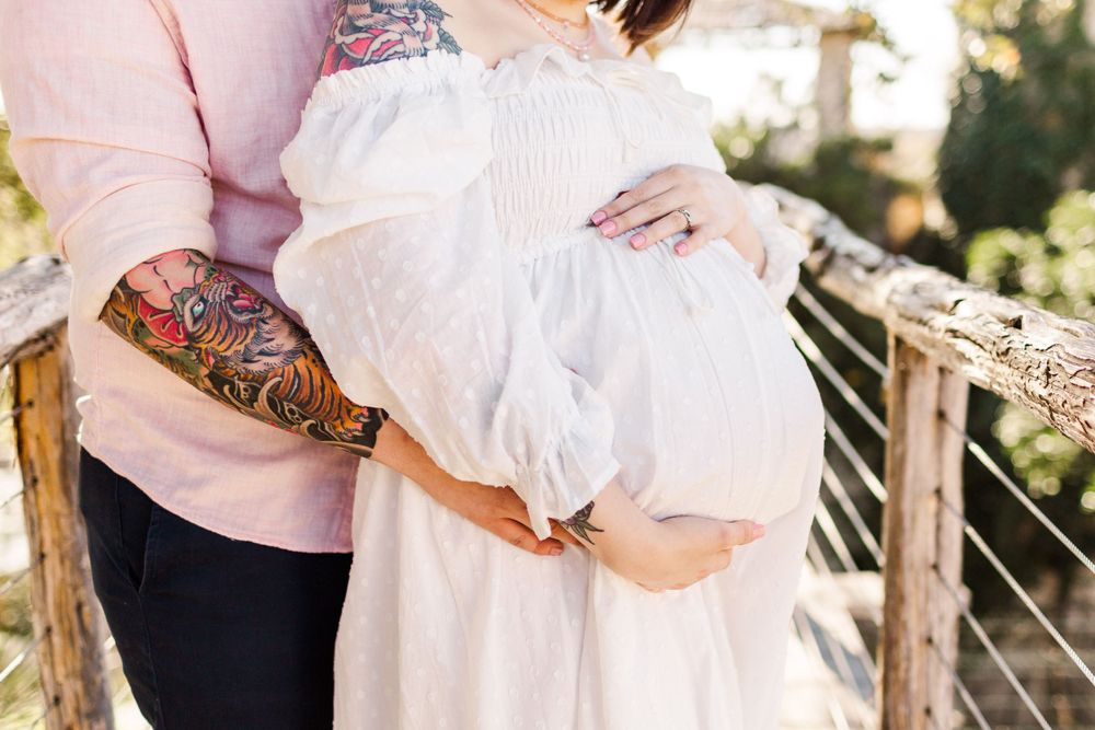 Couple standing together outdoors with tattooed arm embracing maternity bump.