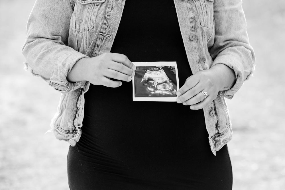 Hands holding an ultrasound photo against a black dress and denim jacket.