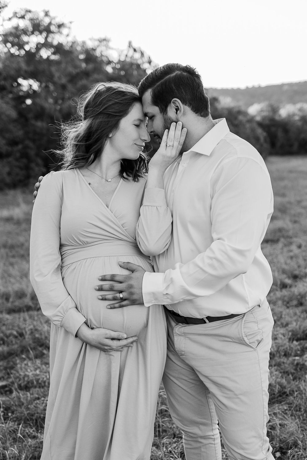 Intimate black and white maternity portrait of couple sharing tender moment outdoors.