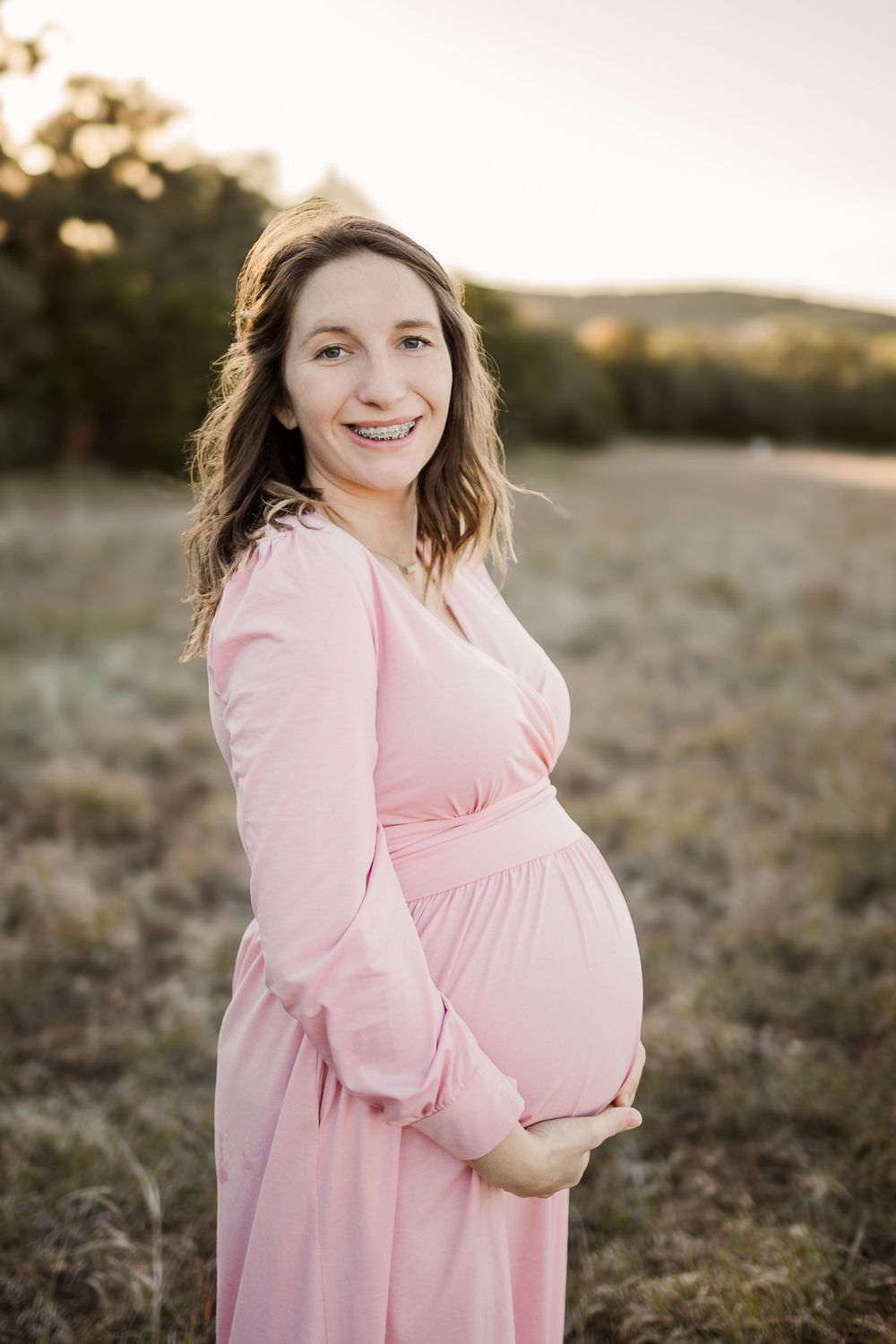 Expectant mother in pink dress poses during golden hour maternity photoshoot.
