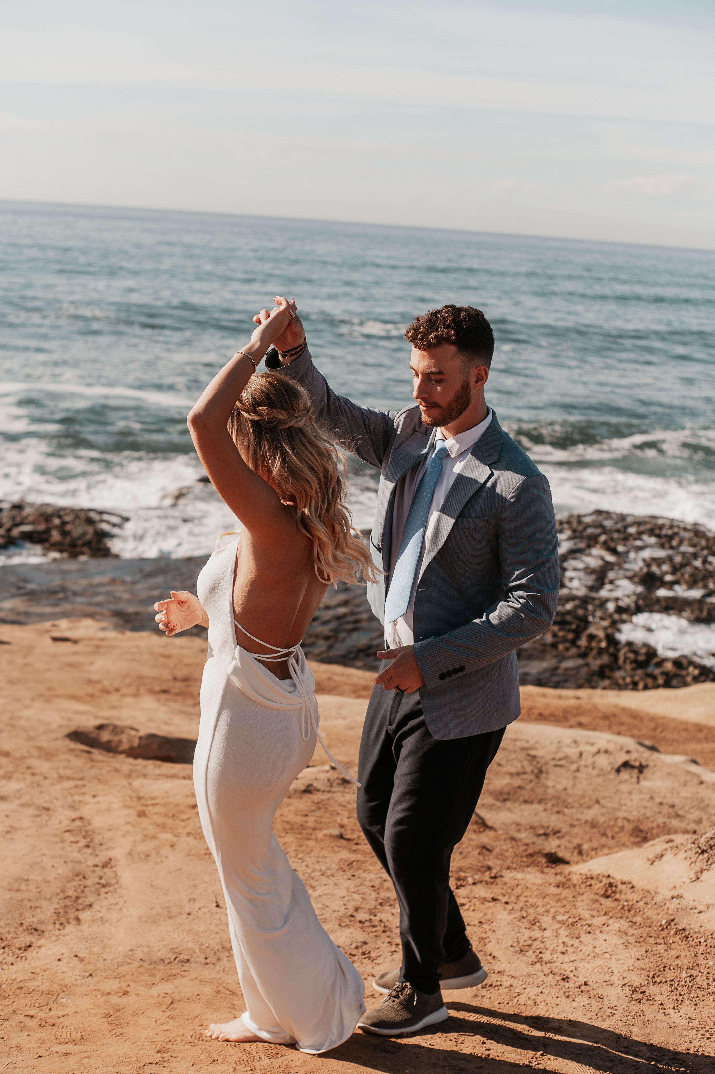 A couple dancing on a coastal cliff overlooking the ocean during a romantic photoshoot.
