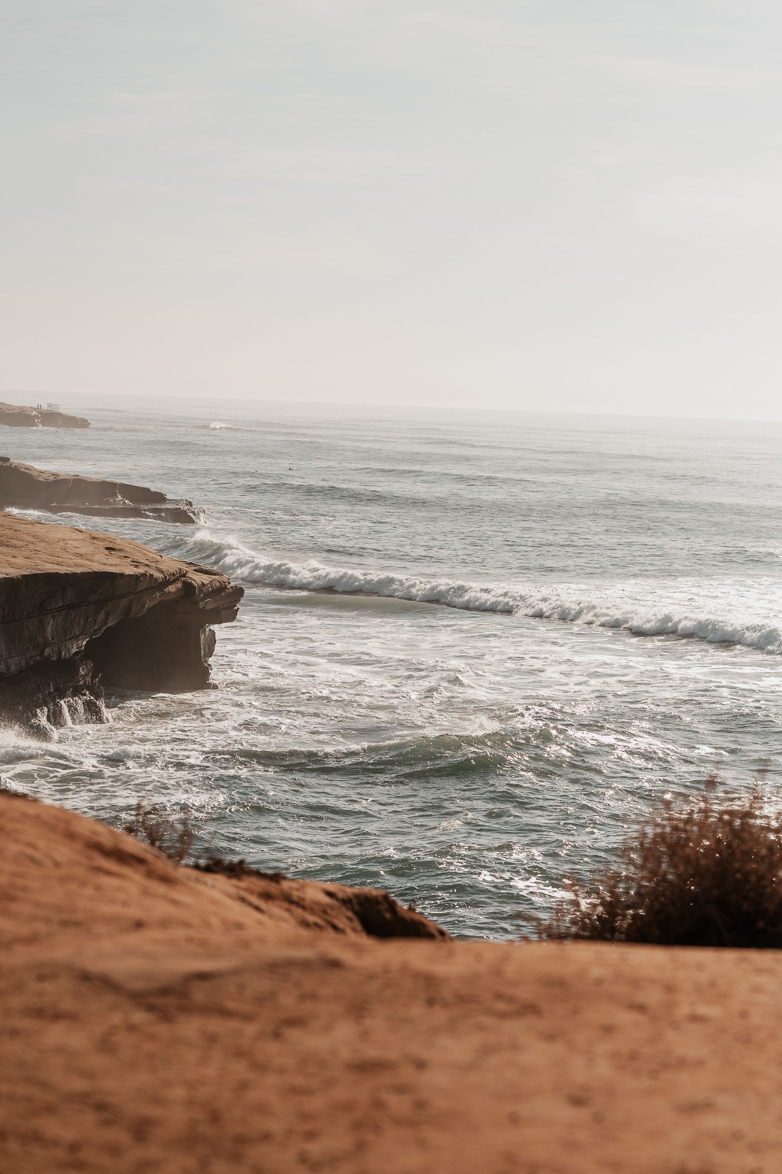 Dramatic coastal landscape with waves crashing against rocky cliffs under an overcast sky.