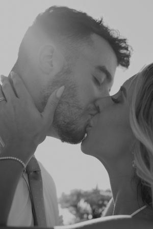 An intimate black and white photo of a couple sharing a kiss outdoors.
