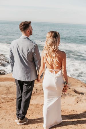 Couple standing at cliff edge overlooking the ocean waves in formal attire.