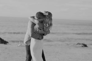 Black and white capture of intimate embrace on oceanside cliff.