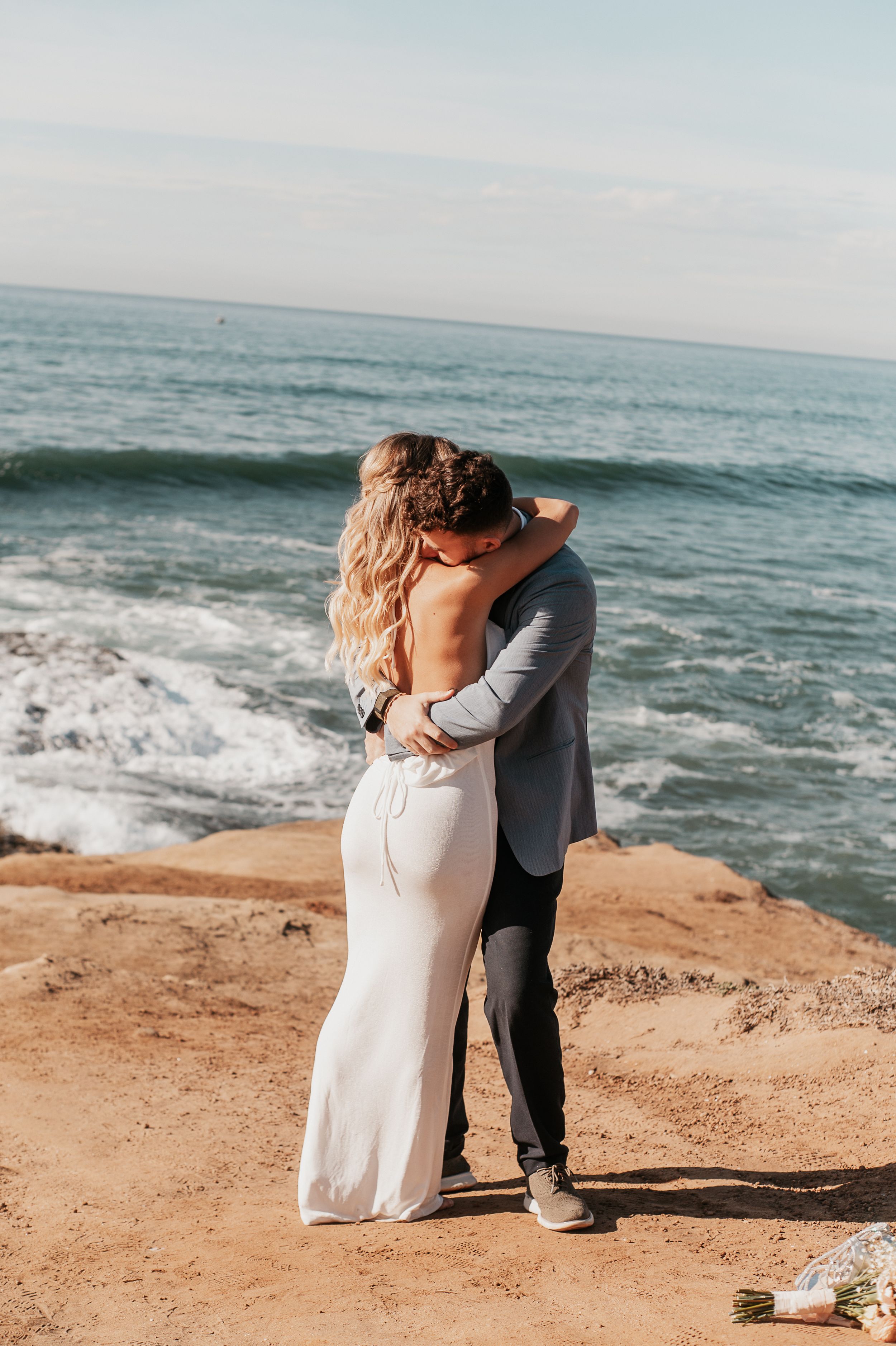 A romantic embrace on a scenic oceanside cliff during a wedding celebration.