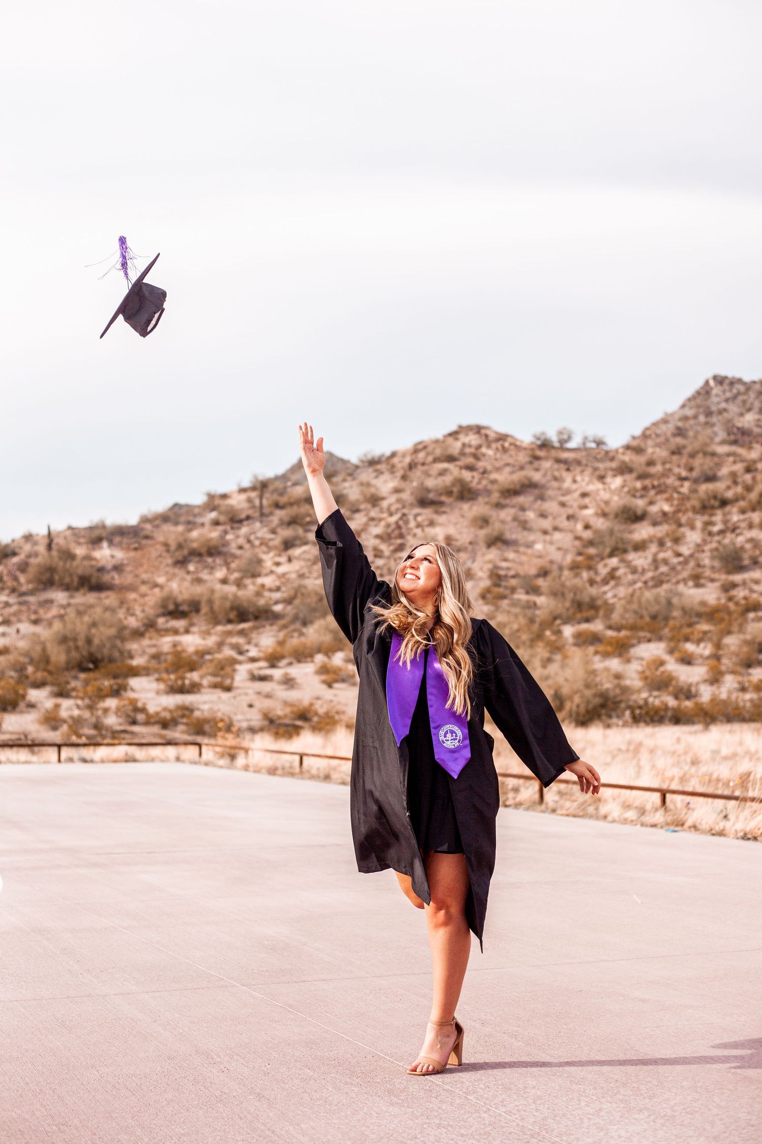 Graduate in cap and gown celebrating with a graceful dance pose in desert landscape.