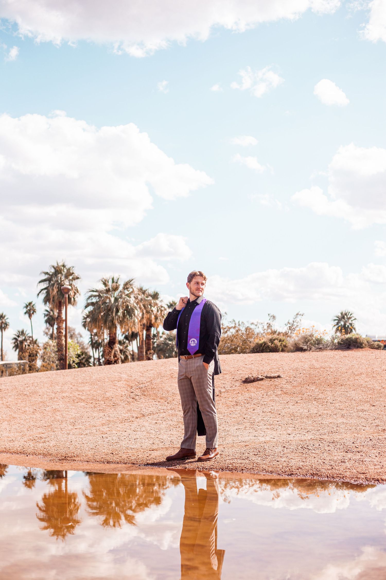 Desert landscape with palm trees and a reflective puddle showing a formal outfit against blue skies.