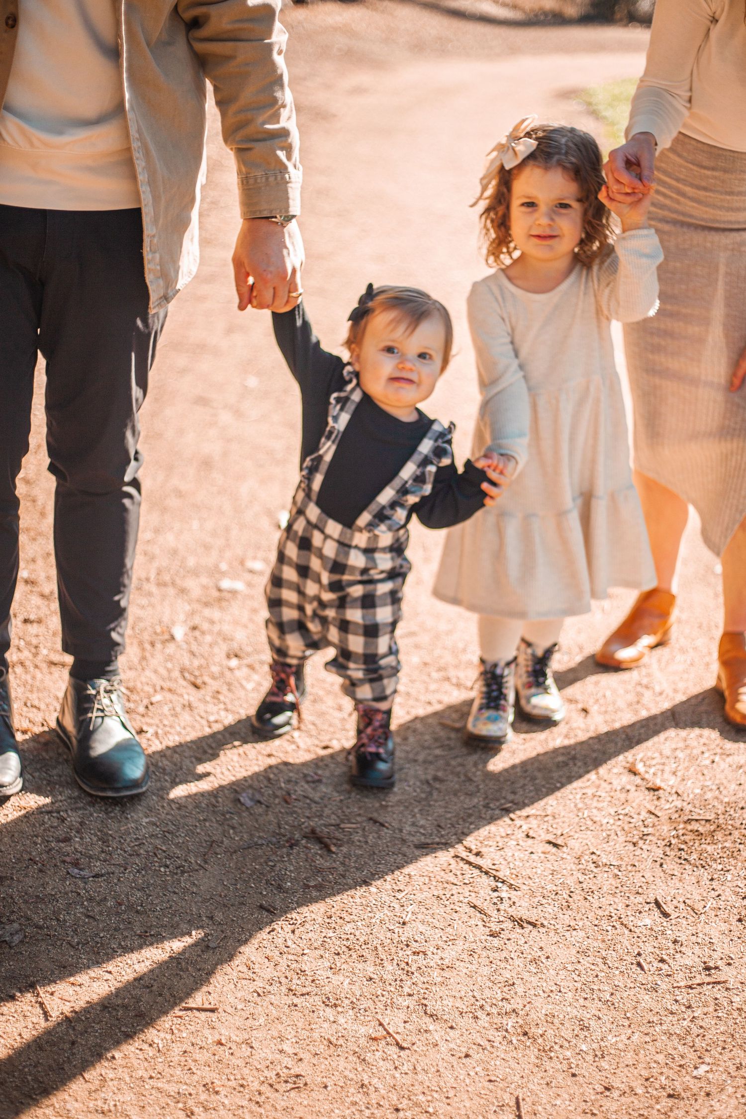 Small children holding hands with parents while walking on dirt path.