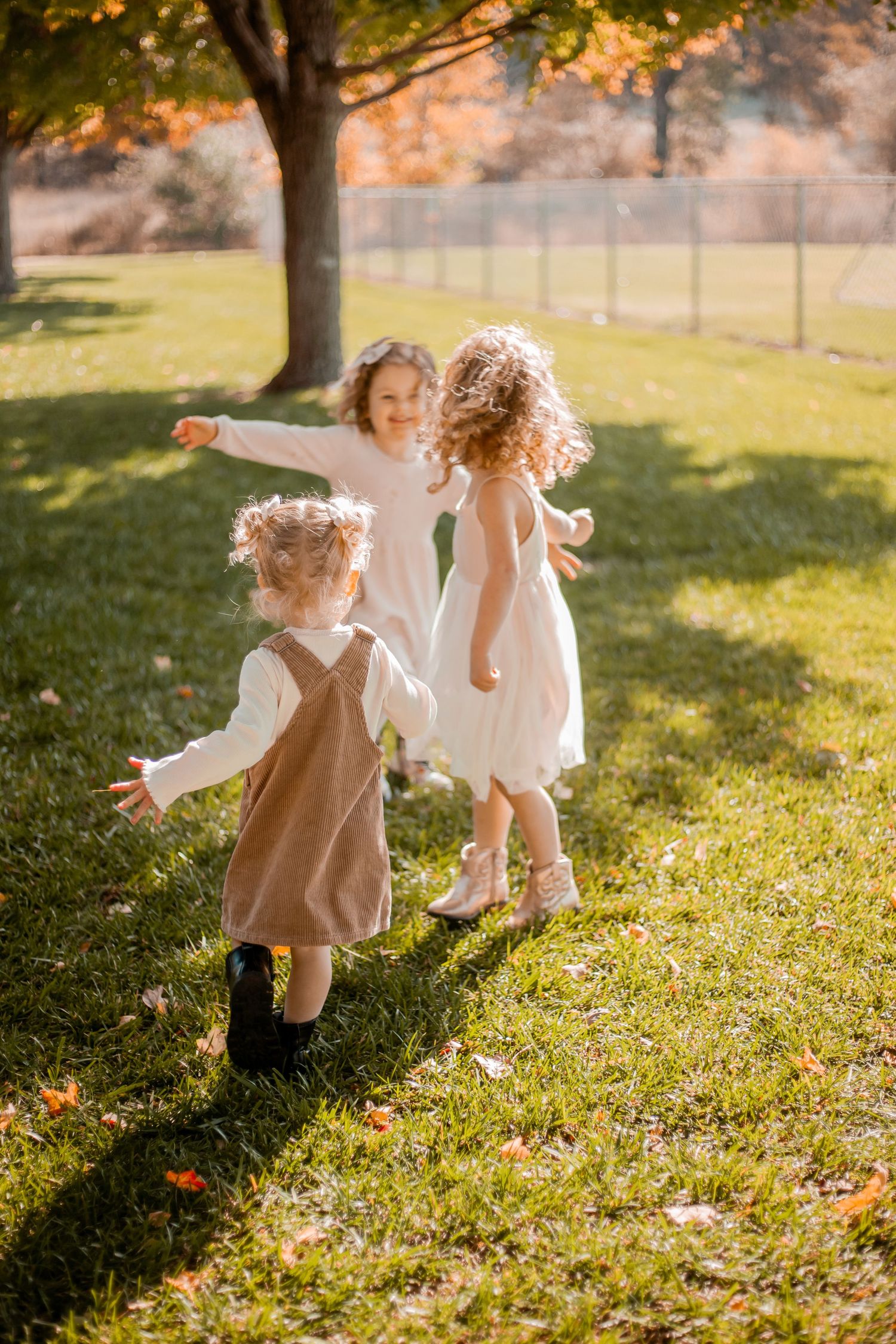 Children in dresses playing and running on grass during golden hour.