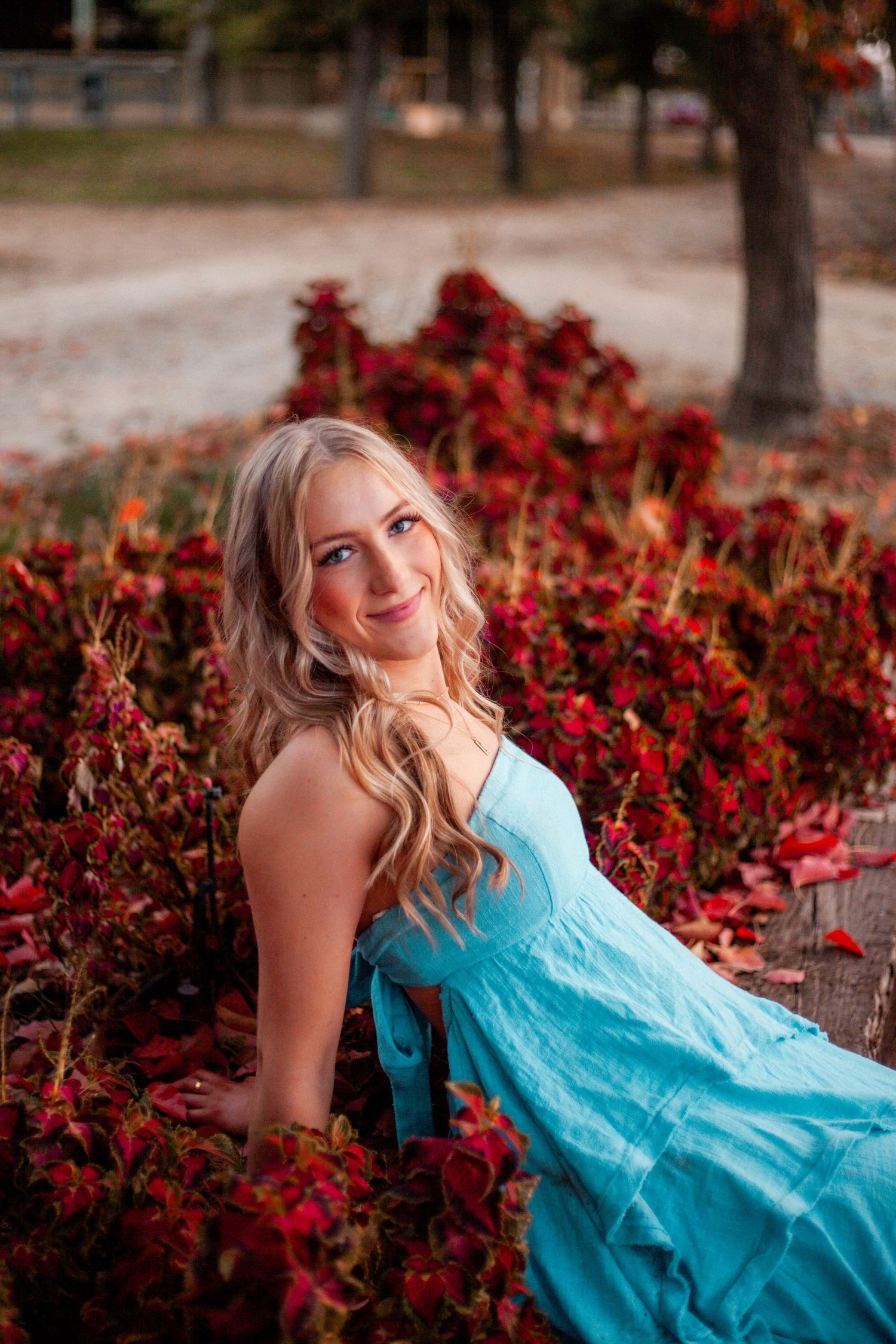 Woman in turquoise dress poses among red autumn foliage.