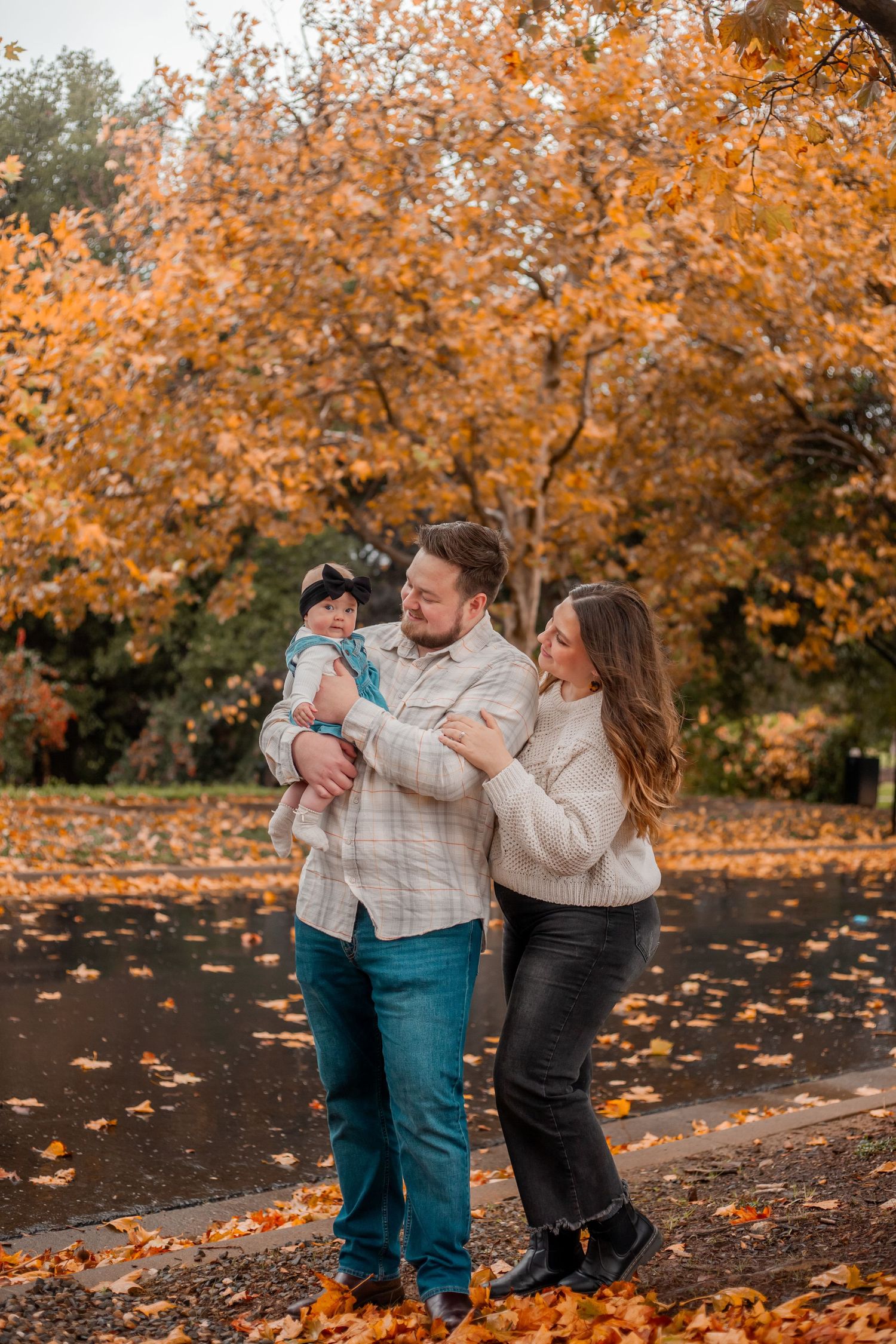 Family embracing under golden autumn trees with fallen leaves.