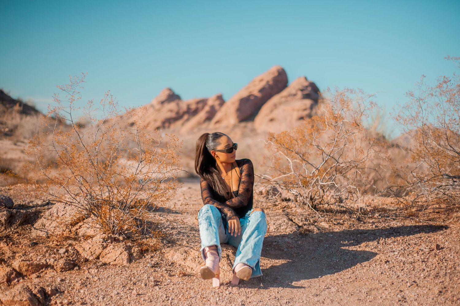 Person sitting on ground in desert landscape with rocky mountains in background.