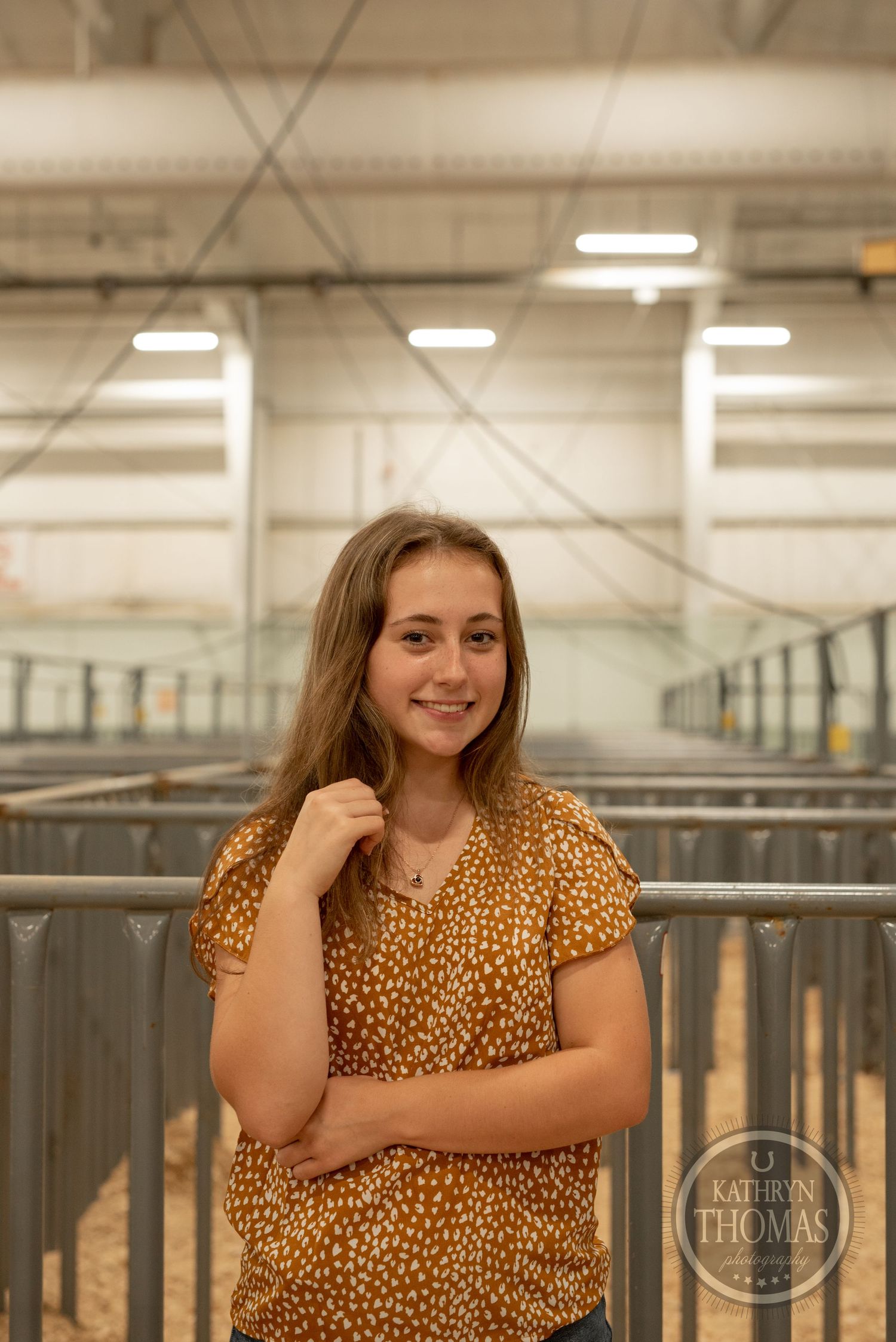 Portrait in livestock facility wearing leopard print top with metal stalls in background.