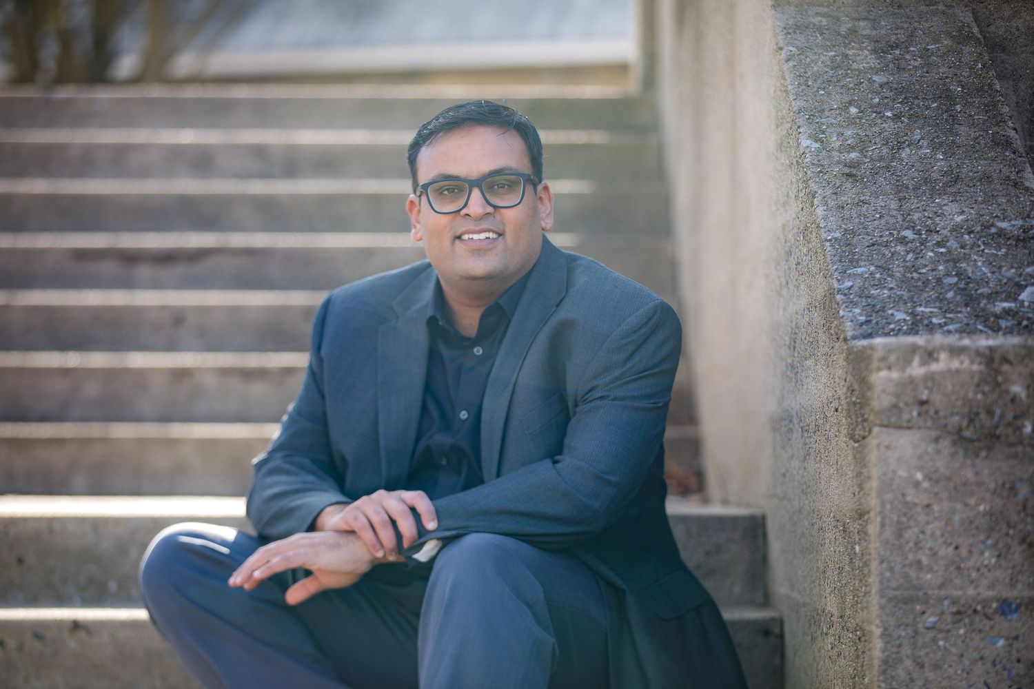 Portrait of a person in business attire sitting on concrete steps.