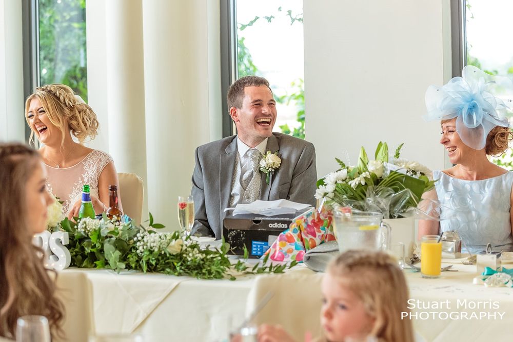 Groom sits down at the top table laughing during the best man’s speech at west tower country house photographer.