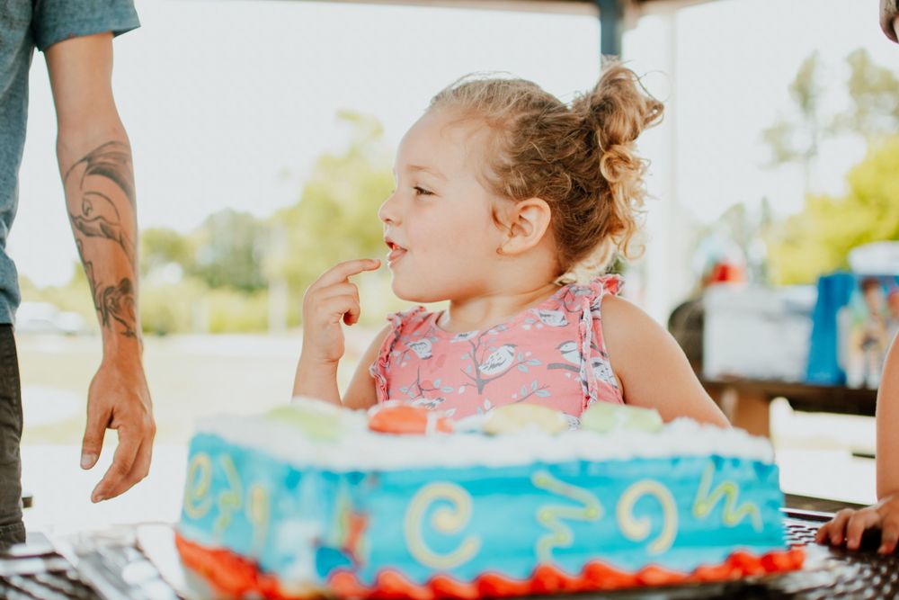 Young child making a wish at a birthday party with blue decorated cake.