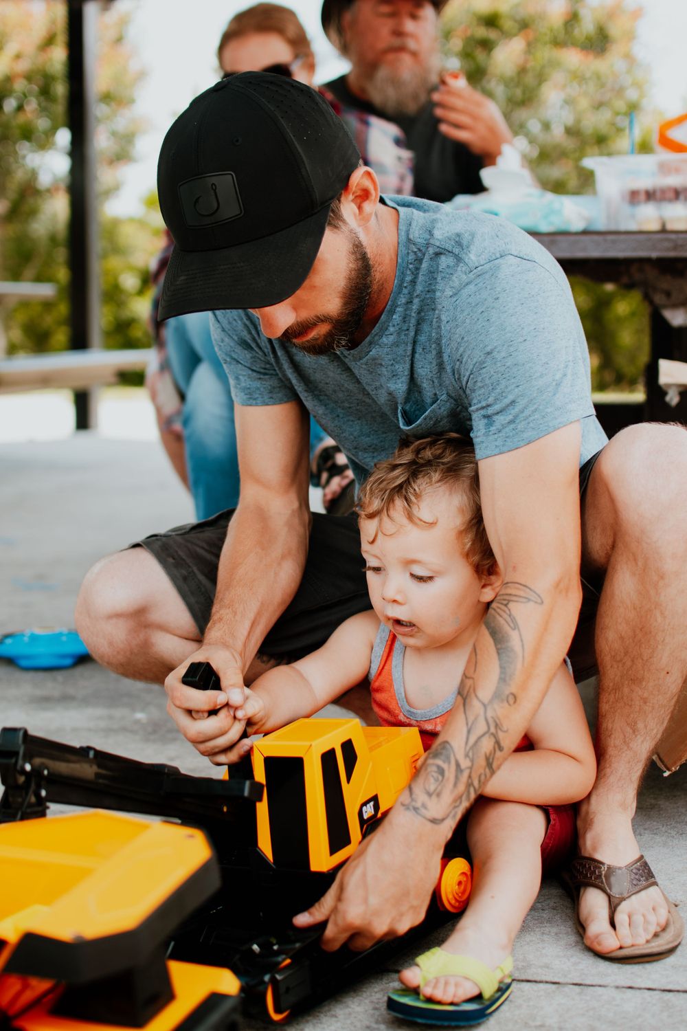 Parent and child examining a yellow toy together at an outdoor gathering.