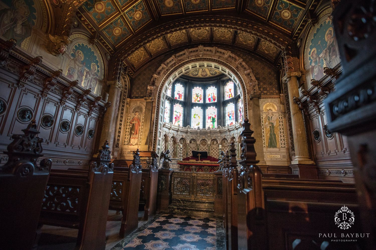 Elegant church altar with stained glass windows and intricate woodwork under vaulted ceiling.