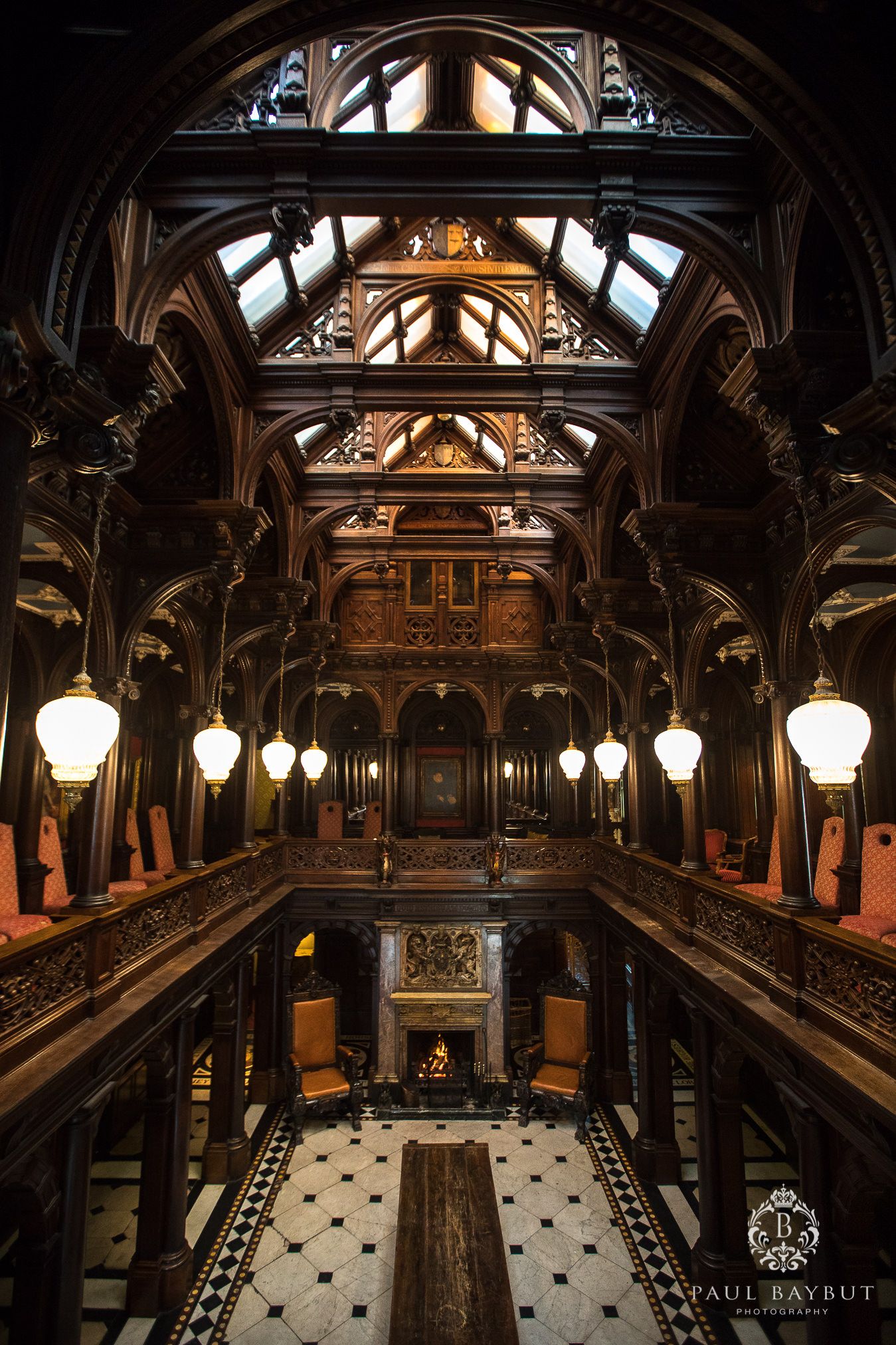 Grand Victorian hall with hanging lanterns and ornate wooden balconies featuring Gothic architectural details.