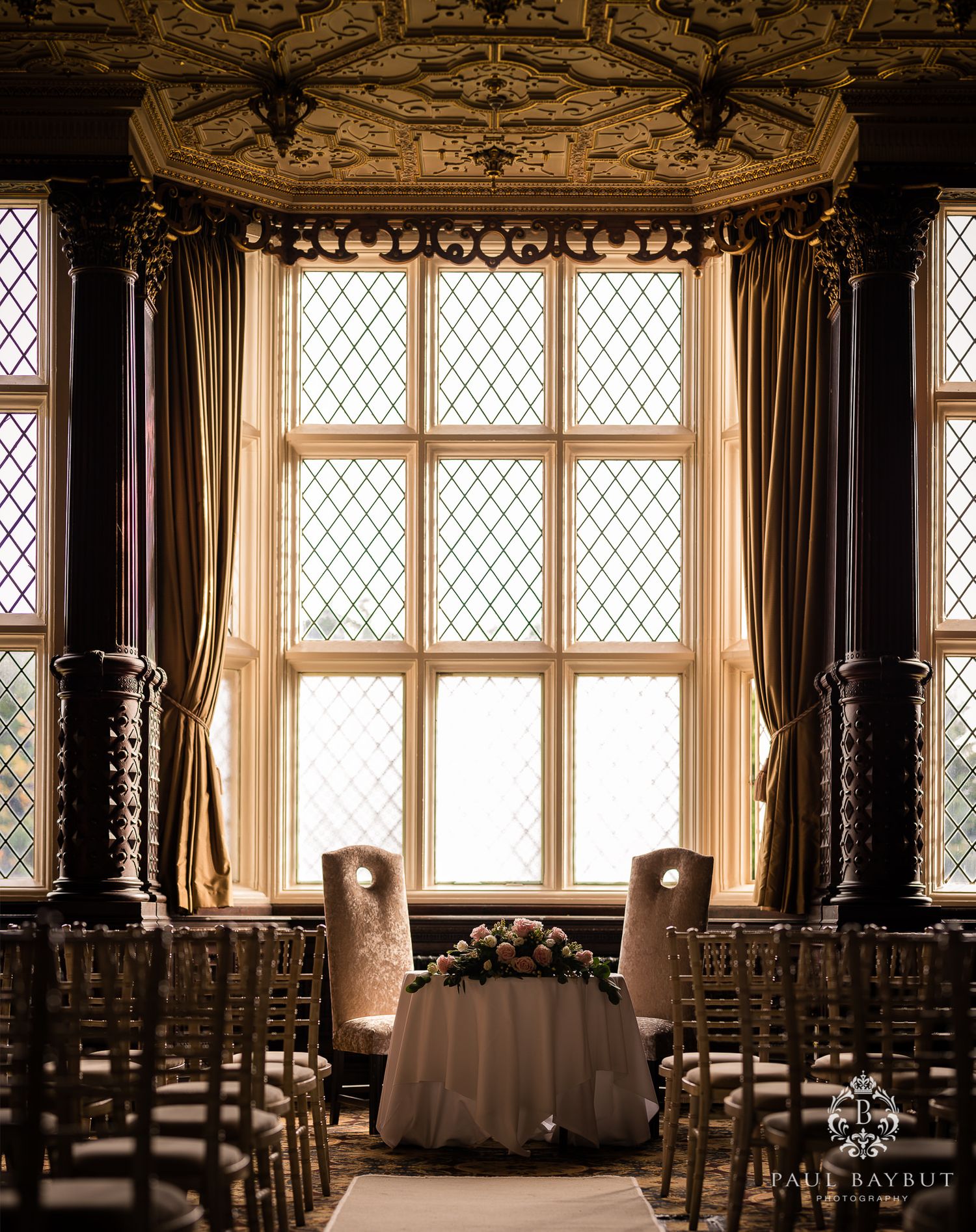 Elegant ceremony setup with draped windows and chairs facing a table in historic room.