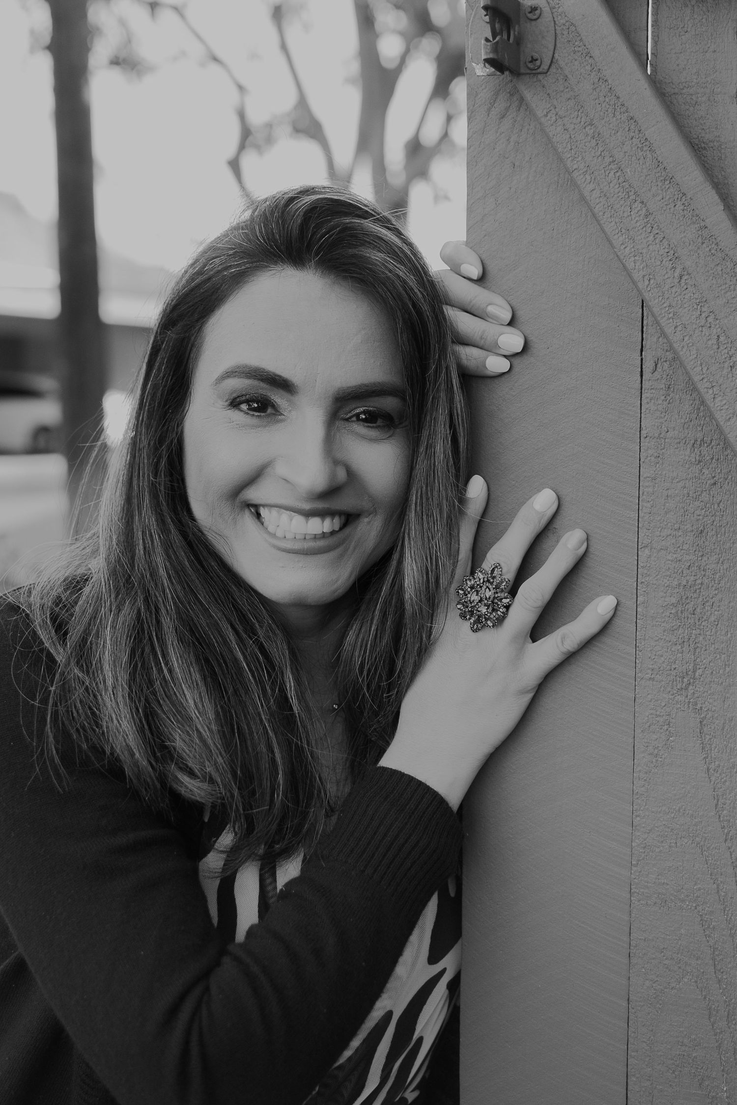 A black and white portrait showing a statement ring and casual style against a wooden wall.