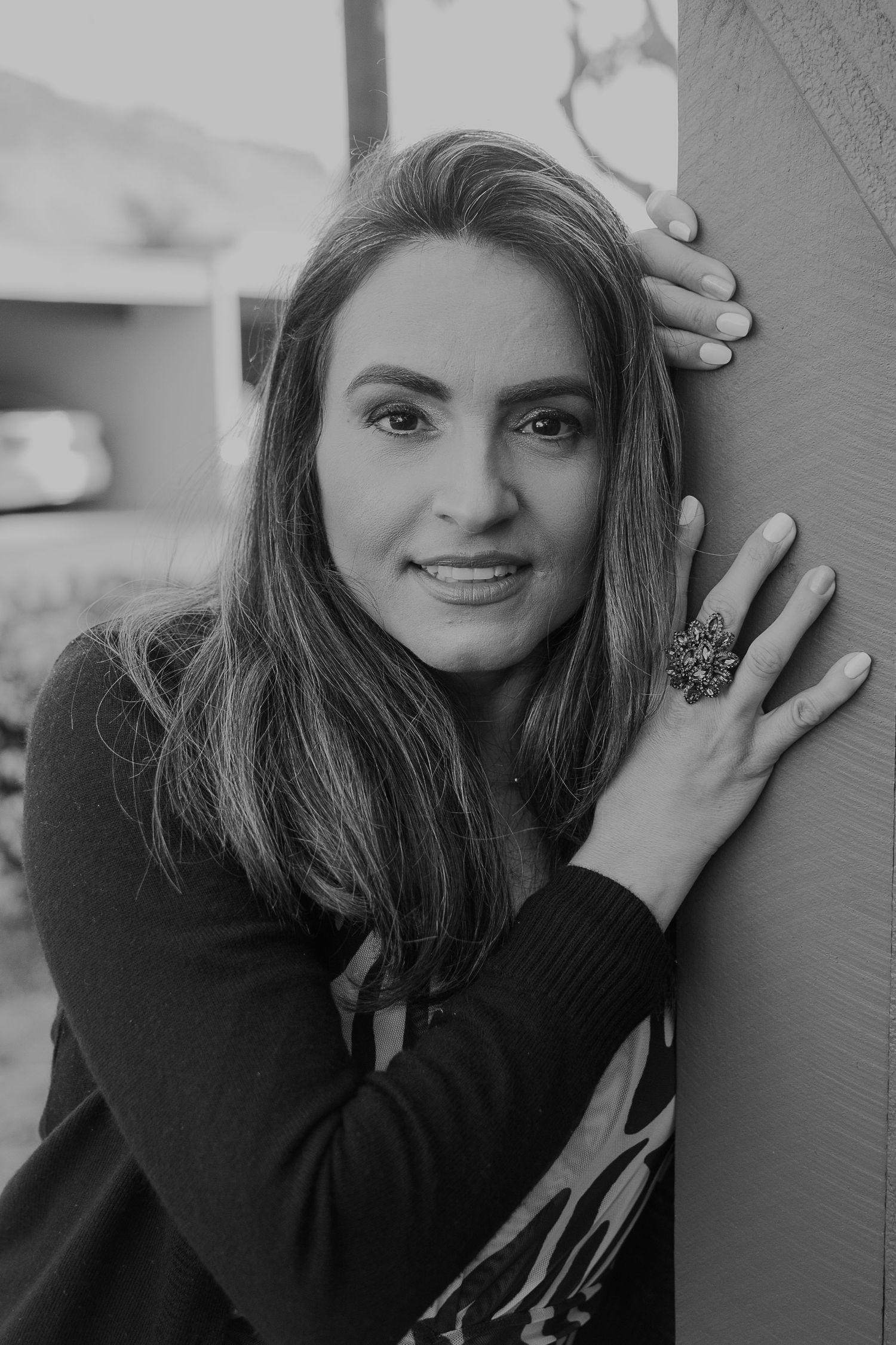 A black and white portrait highlighting a statement ring and relaxed pose against wall.