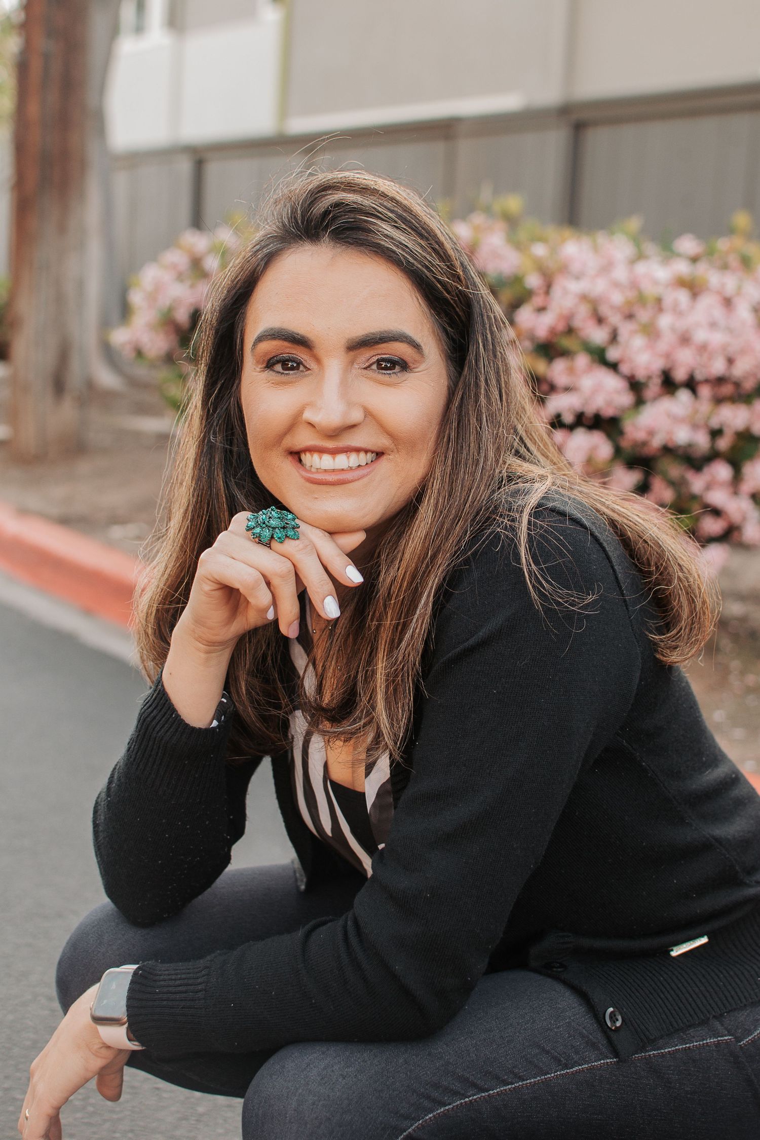 Casual outdoor portrait with flowering pink bushes showcasing turquoise statement ring and black attire.