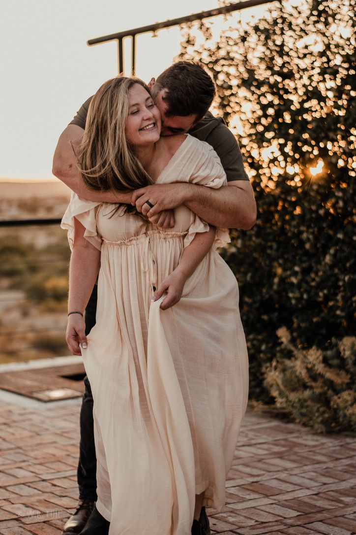 Romantic couple embrace at sunset with glowing bokeh lights in background.