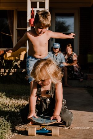 Children playing with a skateboard on porch during golden hour.