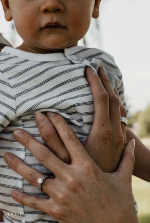 Close-up of hands holding a small child wearing a striped shirt.