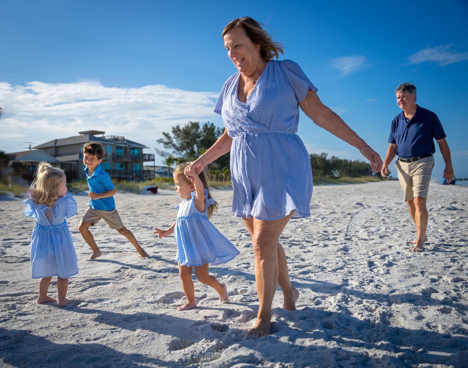 Family group playing and running together on white sandy beach.