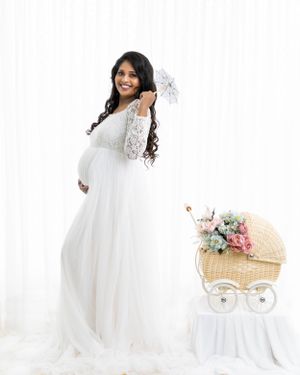 Maternity photo with white lace gown and decorative vintage bassinet on white background.