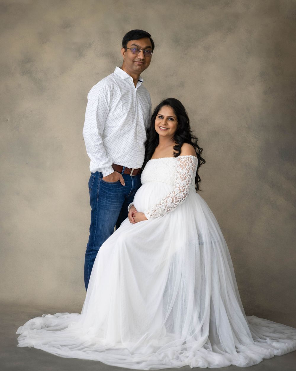 Formal studio portrait of couple wearing white dress and casual white shirt with jeans.